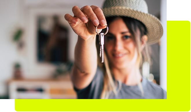 Stolz auf die erste eigene Wohnung zeigt eine junge Frau mit Sonnenhut ihren Schlüssel.