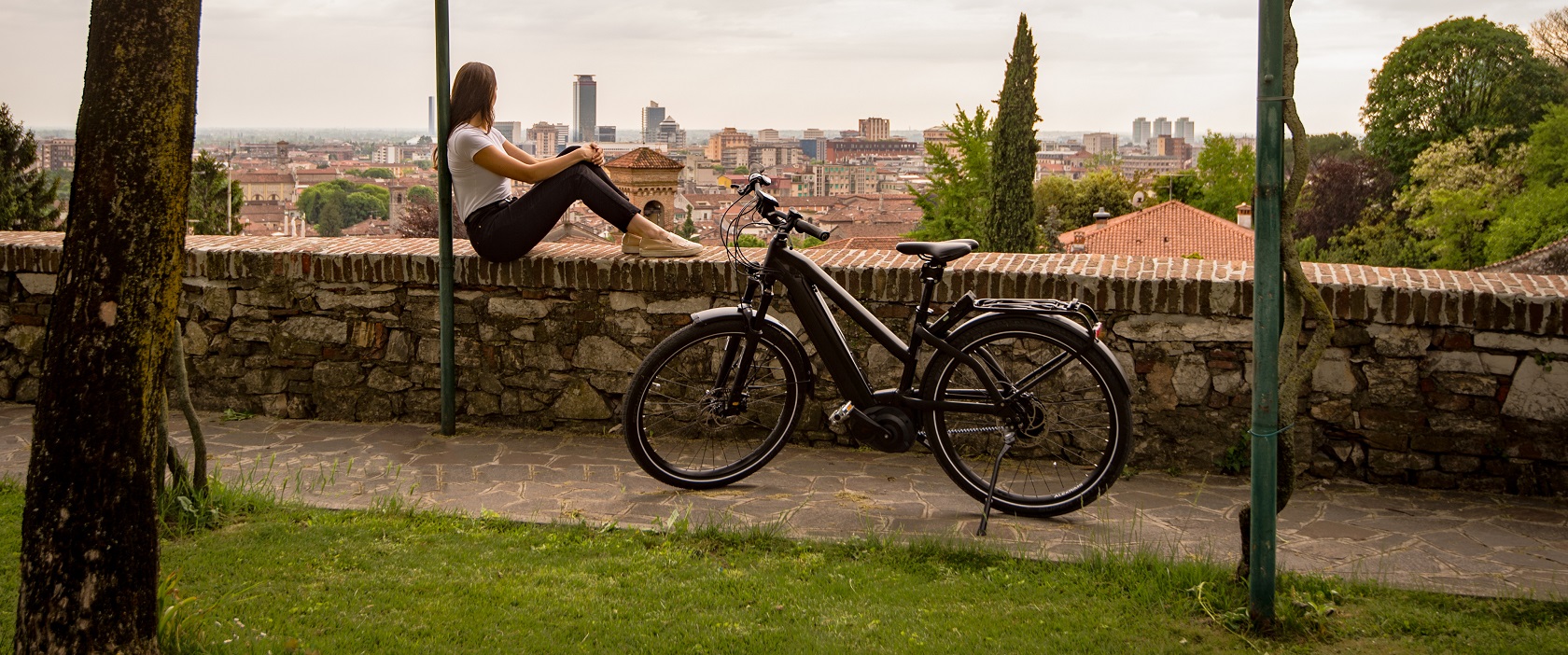 Frau, auf der Mauer sitzend, und E-Bike an der Mauer
