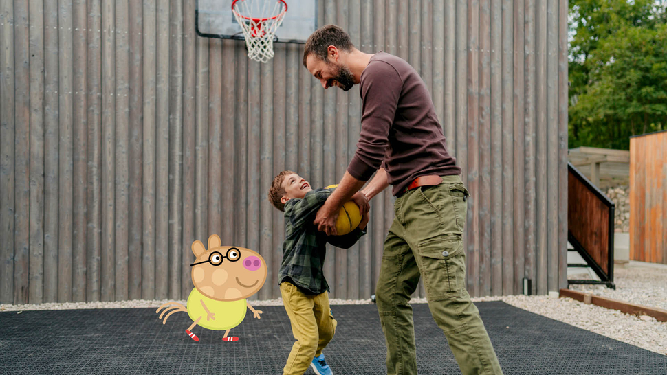 Ein Erwachsener und ein Kind spielen gemeinsam auf einem Basketballplatz, während eine cartoonartige Figur daneben steht.