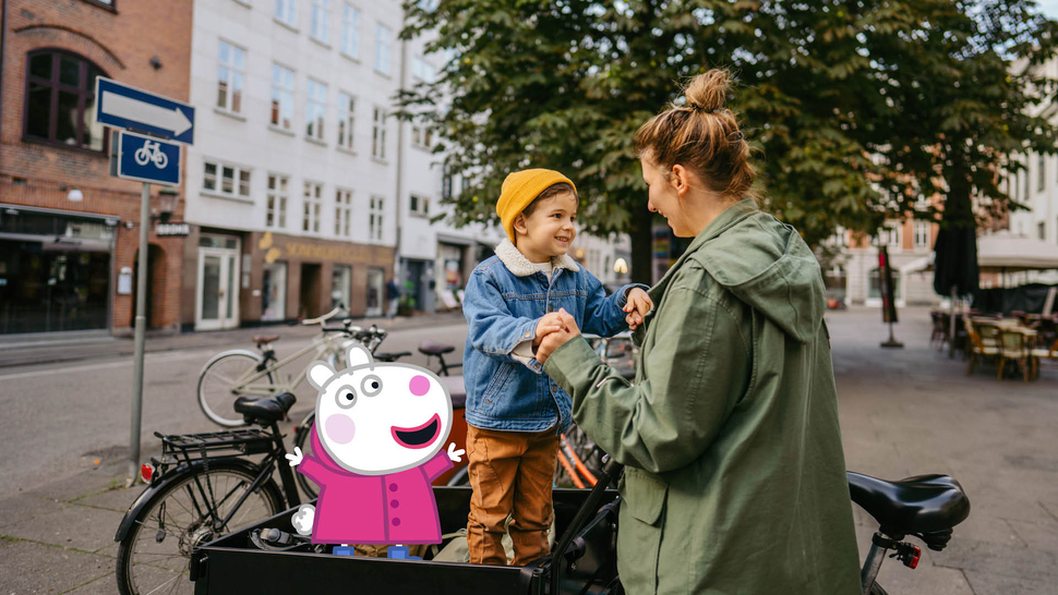 Eine Mutter steht mit ihrem Sohn an einem Fahrrad. Der Junge trägt eine Mütze und schaut lächelnd zu ihr auf.