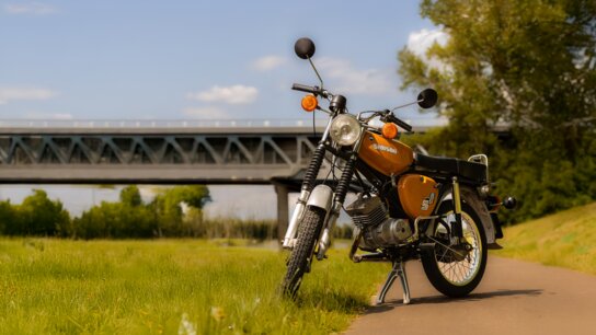 Grauer Roller steht auf einem Feldweg, umgeben von Feldern und unter bewölktem Himmel.