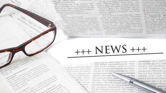 Brille und Füller liegen auf Zeitungen mit dem Wort „NEWS“ prominent in der Mitte.