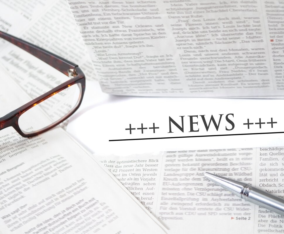 Brille und Füller liegen auf Zeitungen mit dem Wort „NEWS“ prominent in der Mitte.