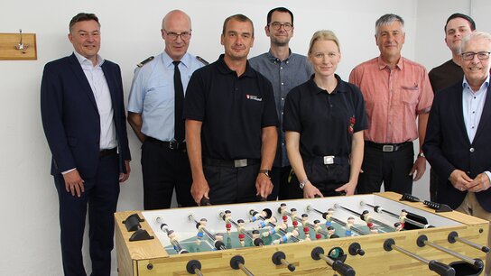 Gruppe von sieben Personen, die um einen Tischfußballtisch stehen, im Hintergrund eine helle Wand.